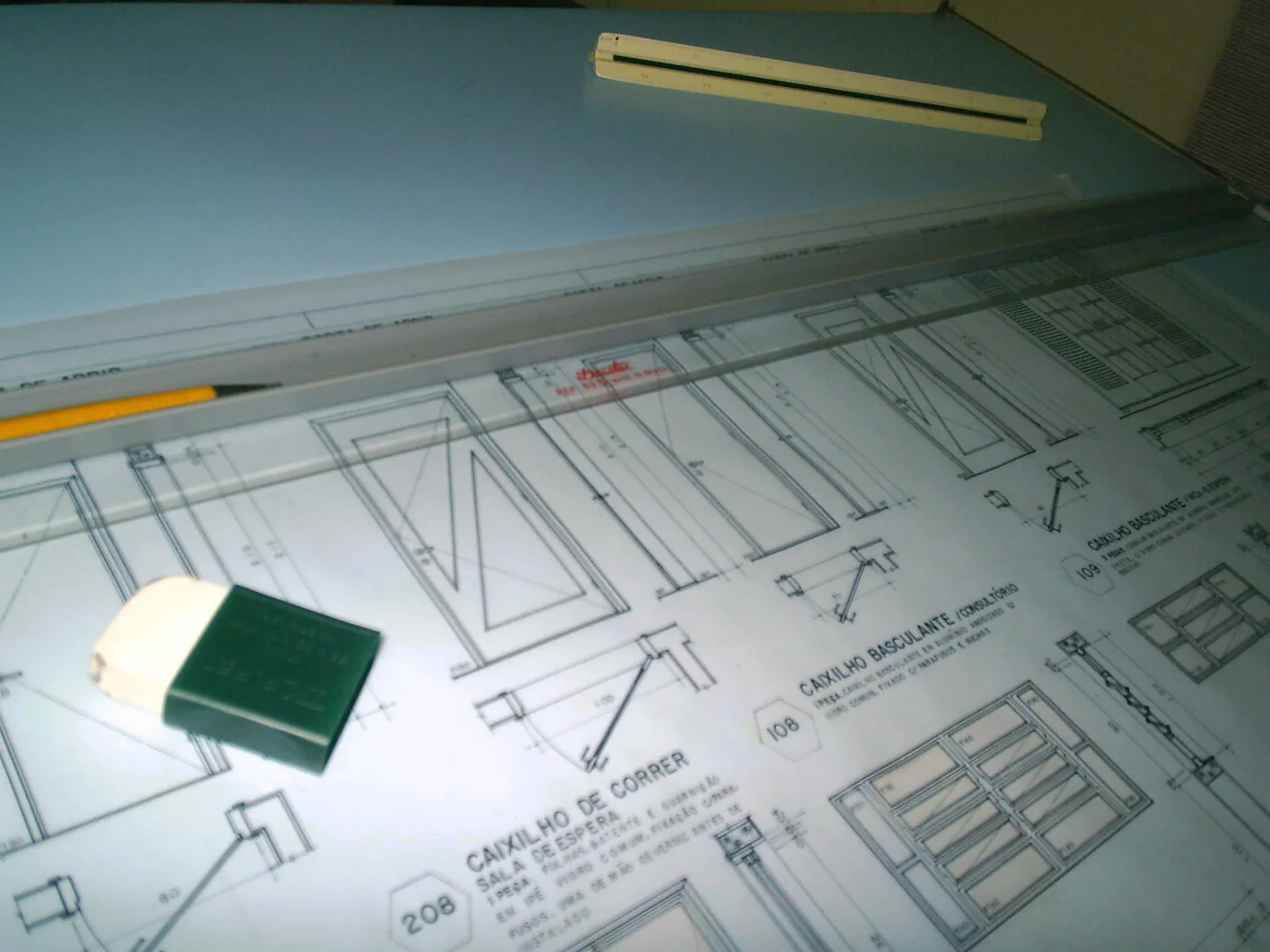 Fotografía referencial de planos de detalles constructivos sobre una mesa de dibujo, con regla, lápiz y goma.