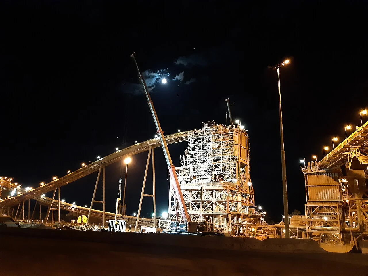 Fotografía referencial: edificio de chancado secundario con andamios, grúa móvil y correas transportadoras durante una parada nocturna de mantenimiento.