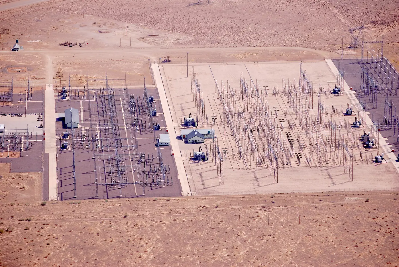 Imagen ilustrativa: vista aérea de un patio de alta tensión con transformadores, barras y estructuras metálicas en terreno árido.