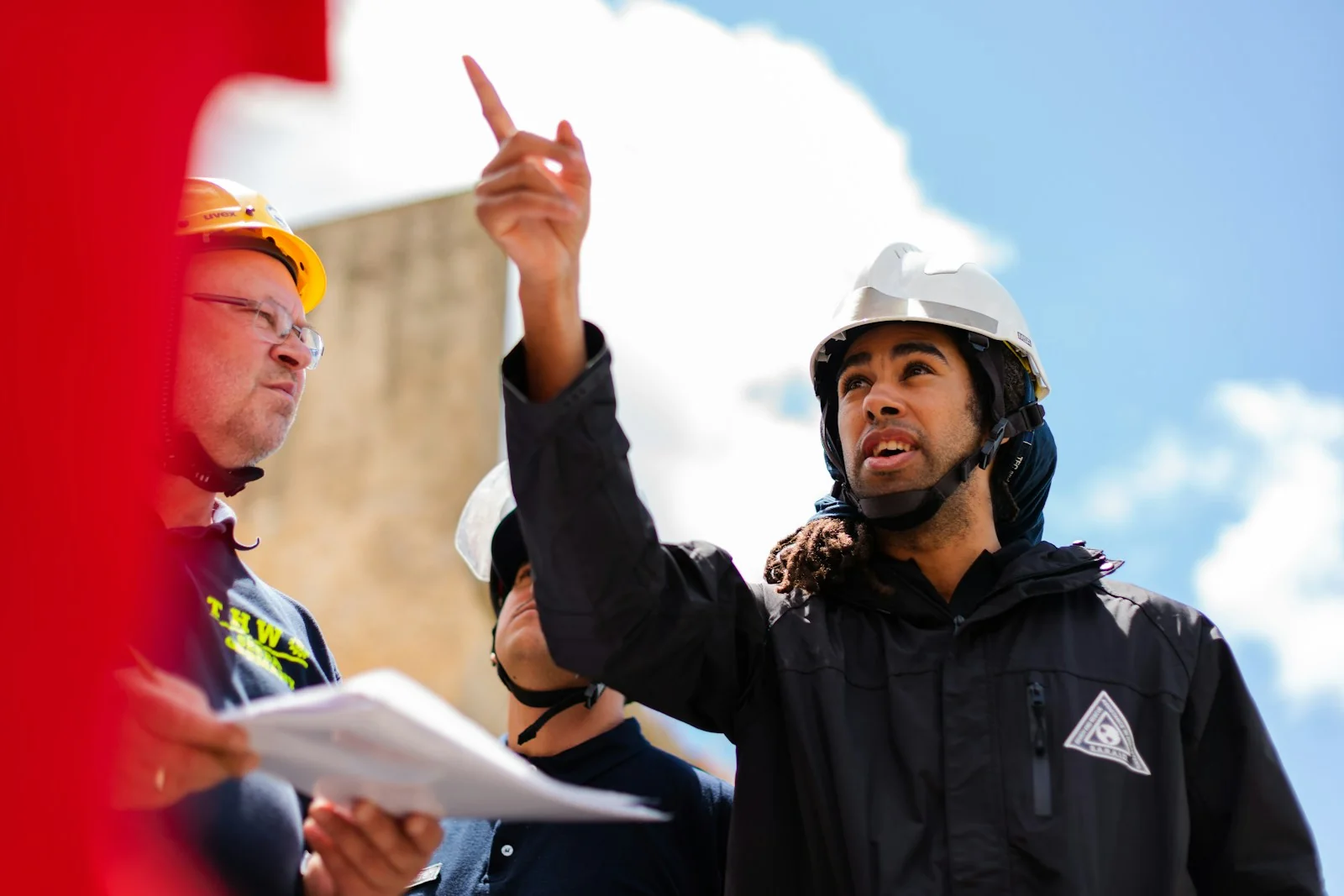 Ingenieros con cascos revisan planos y señalan una estructura en obra. Fotografía referencial.