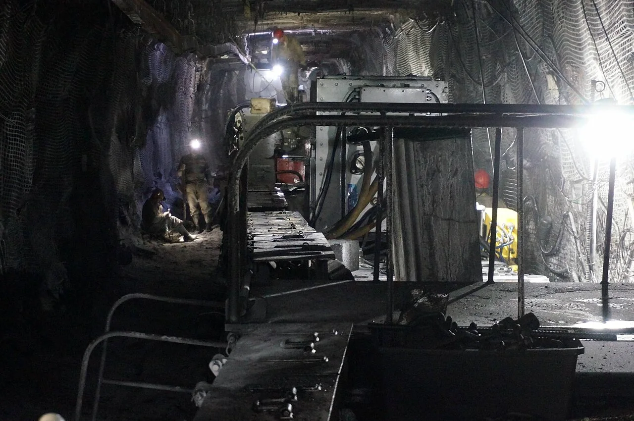 Imagen ilustrativa: maquinaria, sostenimiento y trabajadores en una galería minera subterránea.